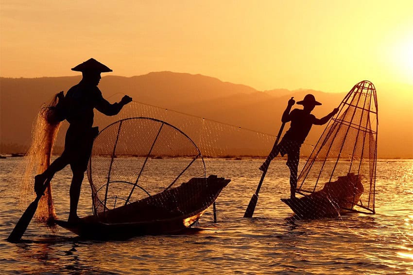 Two fishermen casting their net into the ocean